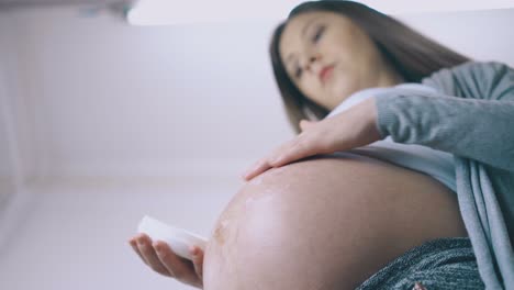 임신 한 여자 는 배 를 가까이 들여다보면서 수분 로션 을 사용 한다