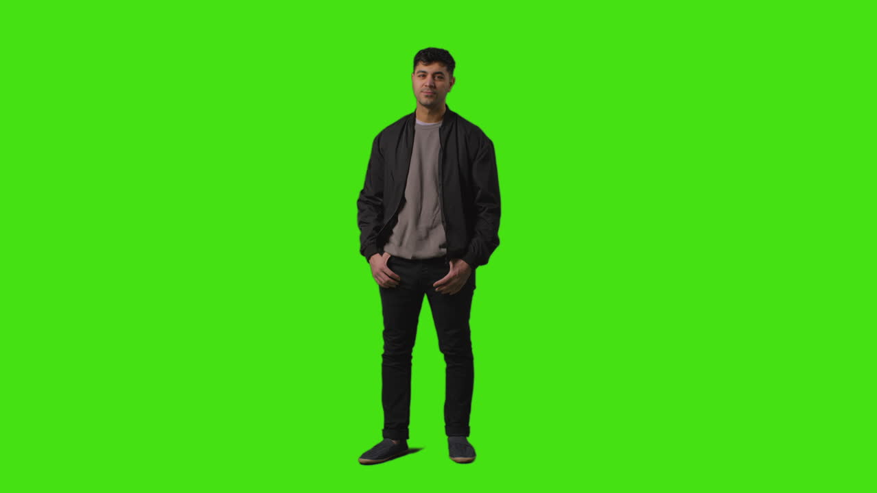 주머니에 손을 넣고 녹색 스크린에 서있는 비정상적으로 옷을 입은 젊은 남자의 전체 길이  1