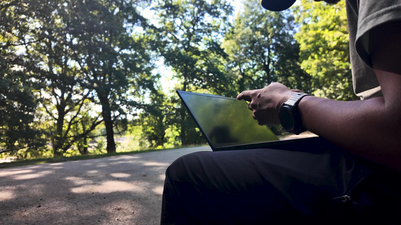Freelancer using laptop sitting in a park enjoying the sunny day and remote working