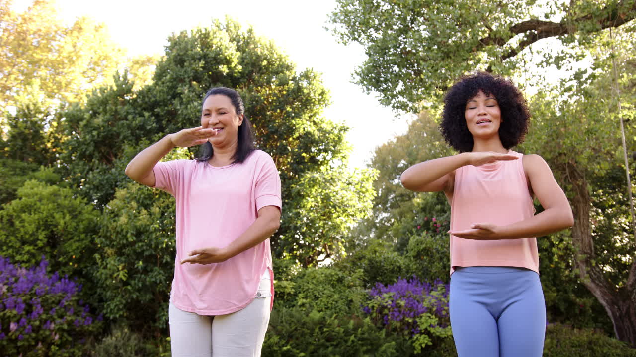Practicing tai chi, mother and adult daughter smiling and enjoying outdoor exercise in park