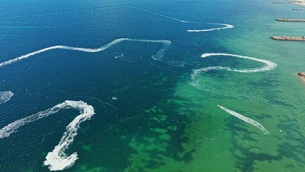 Güneşli bir günde, okyanusun berrak sularında belirgin izler bırakarak jet ski yarışı.