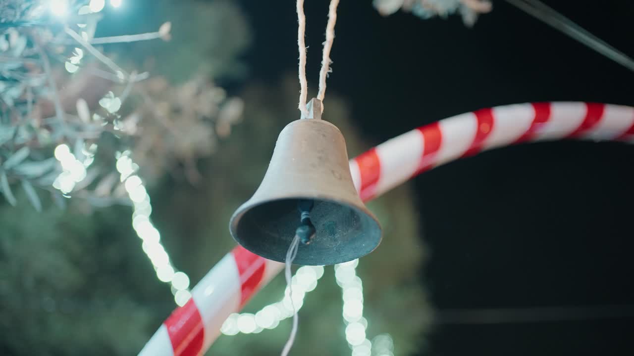 metal bell hanging outdoors with candy cane decorations and soft festive lighting