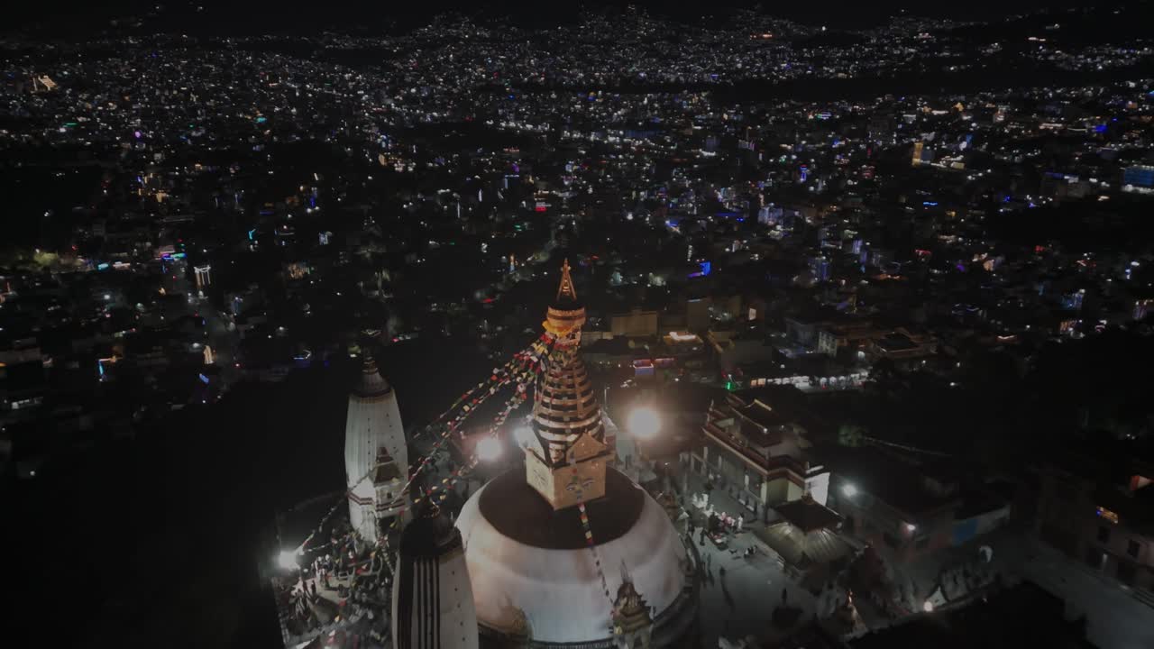 Aerial night drone footage of Swayambhunath Stupa in Kathmandu, glowing with warm lights and surrounded by the peaceful cityscape, showcasing Nepal’s iconic Buddhist heritage and nighttime beauty