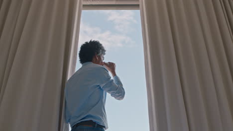 young man drinking coffee in hotel room looking out window planning ahead enjoying view of ocean