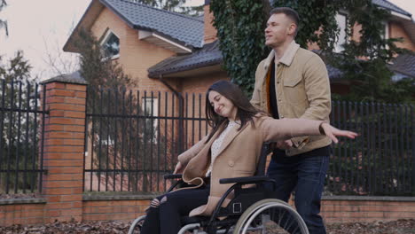 side view of a man taking her disabled friend in wheelchair on a walk around the city 1