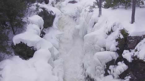 Aerial-drone-view-of-a-frozen-waterfall-nestled-in-a-wintry-forest-landscape-surrounded-by-trees