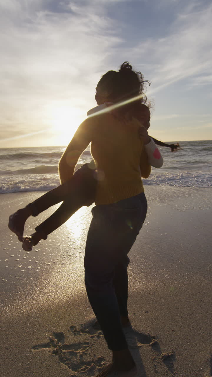 video vertical de madre biracial con hija jugando en una playa soleada