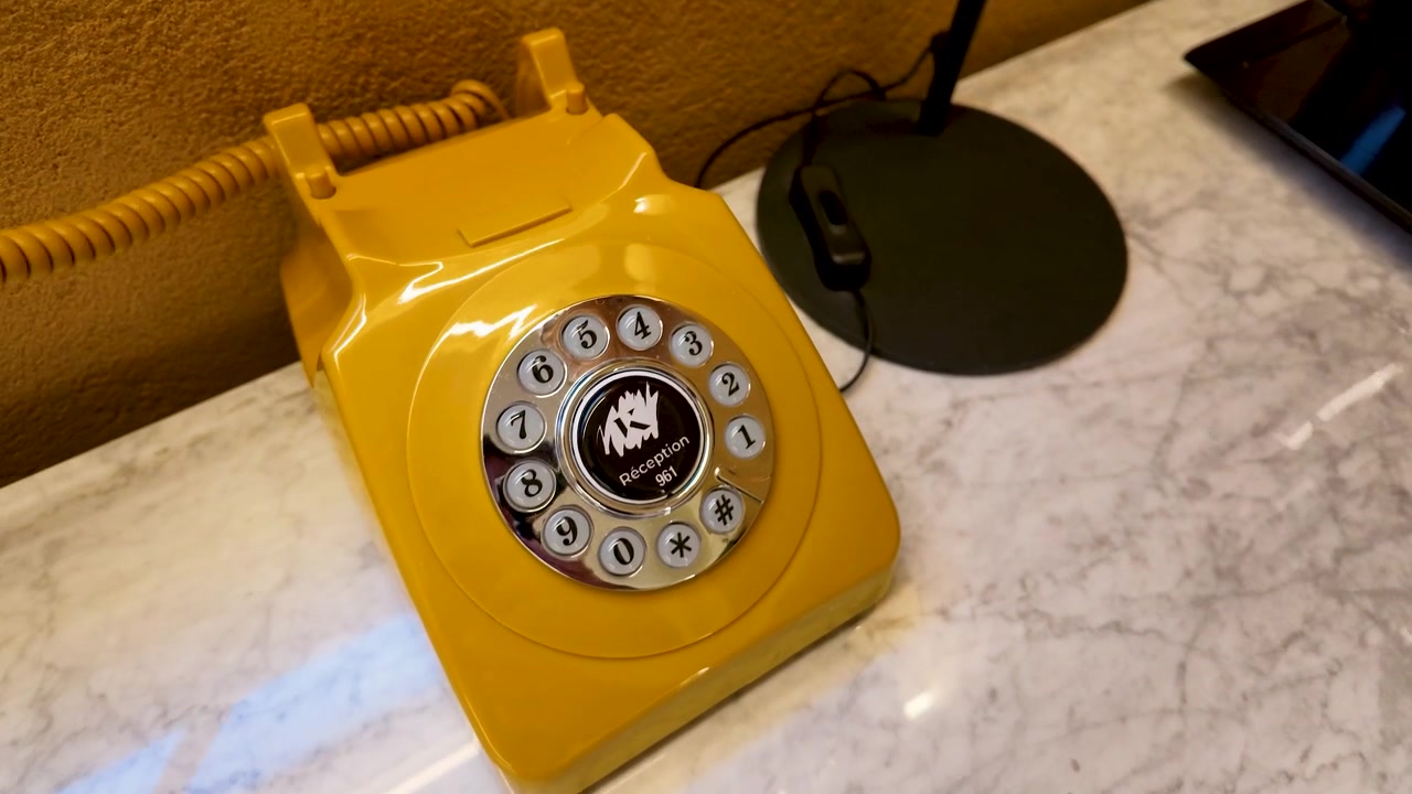 Una mano prende un telefono a disco giallo vintage su un bancone della reception di un hotel in marmo