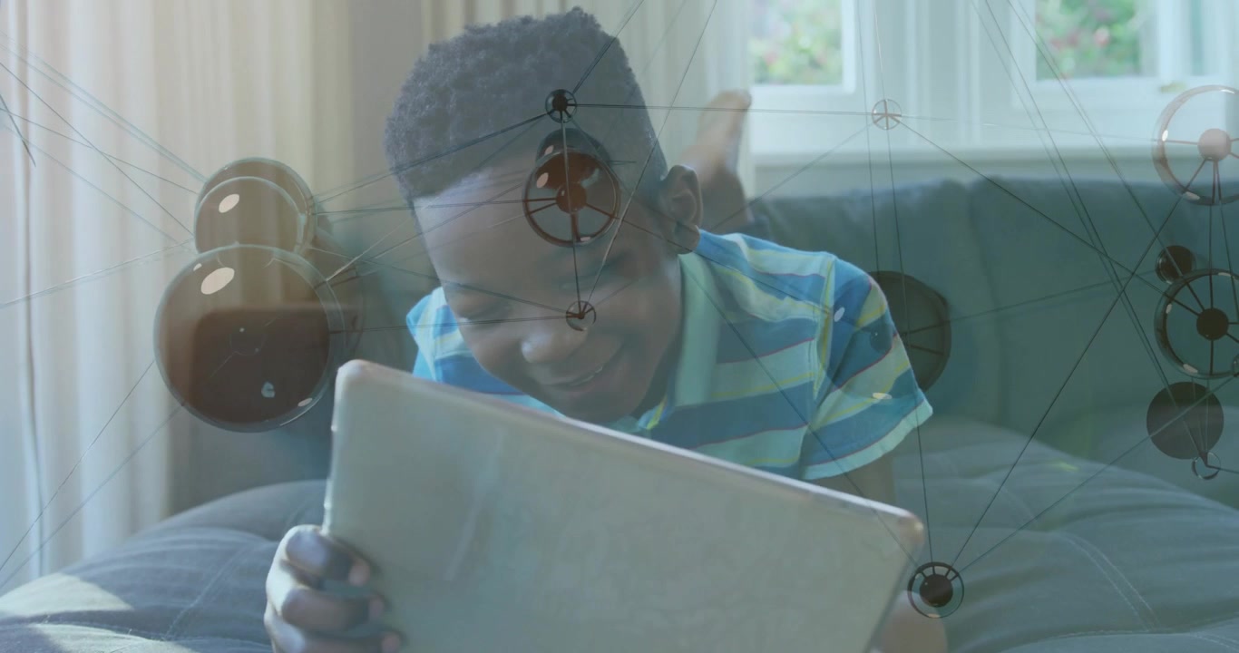 Laughing child in striped polo leaning on living room sofa, holding tablet and overlay graphic