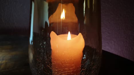 llama de vela naranja gruesa ardiendo y parpadeando en un hermoso jarrón de flores de vidrio agrietado sobre una mesa de madera