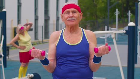 anciano abuelo haciendo entrenamiento de levantamiento de pesas haciendo ejercicios con pesas en el patio de recreo en el parque