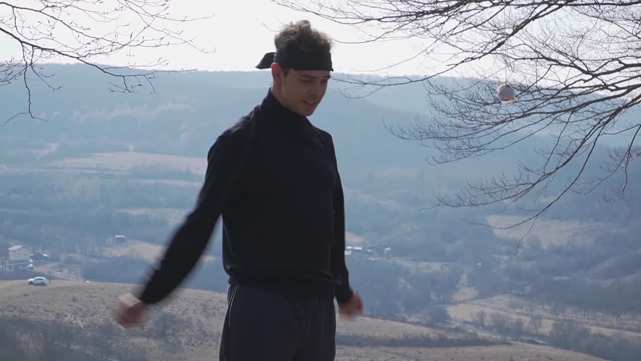 A young man dressed in black with a headband stretches his arms on a mountain cliff. Ideal theme for fitness, sports, well-being.
