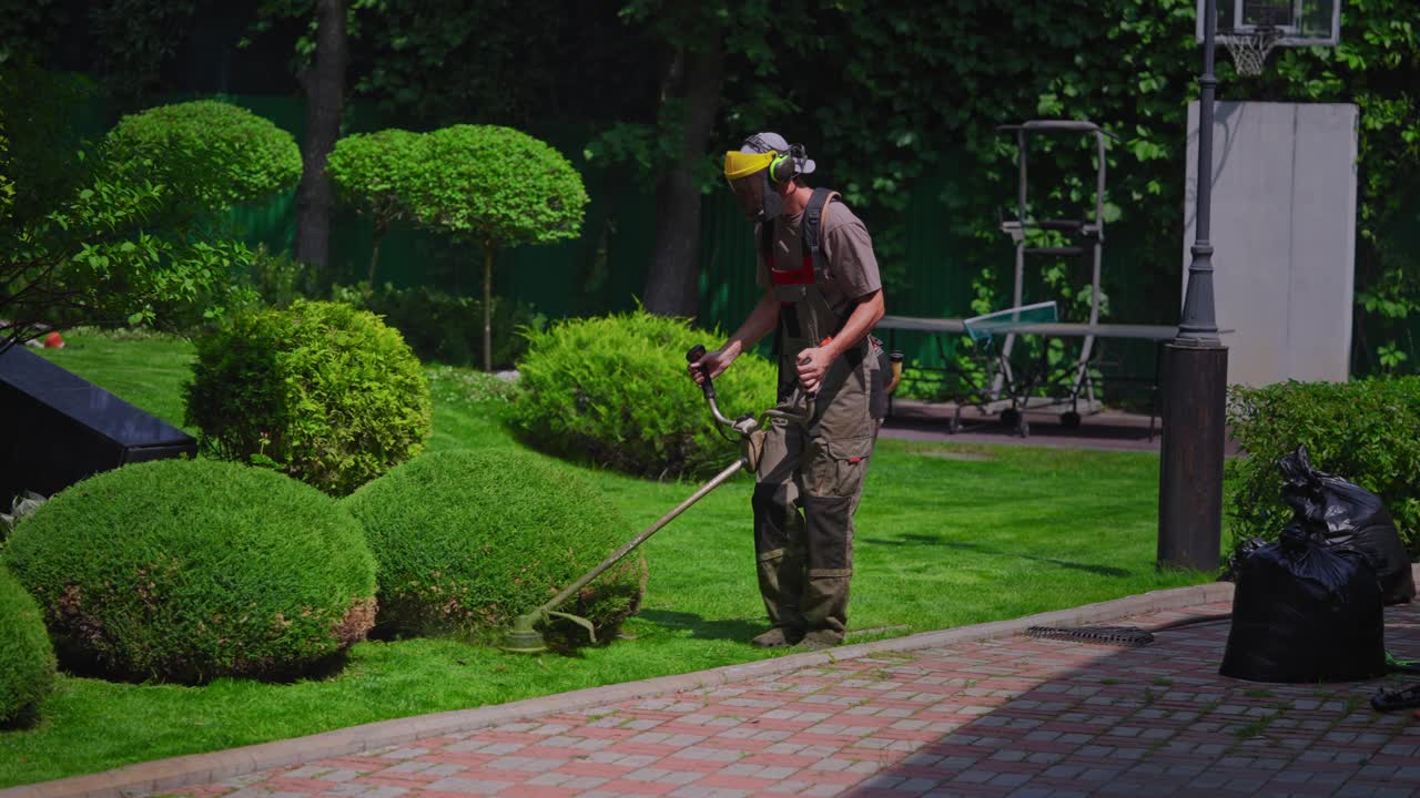 Jardinero profesional recortando los bordes del césped con una desbrozadora de hilo en un patio soleado