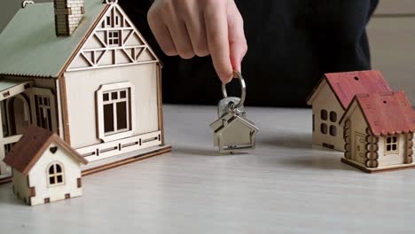 llavero con las llaves de la casa en la mano. casas de juguete en la mesa. compra de bienes raíces. transacción inmobiliaria