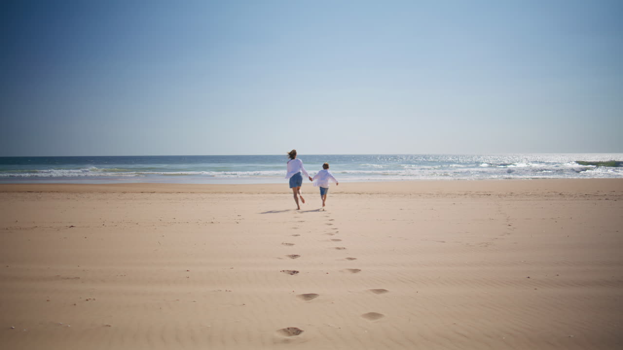 Happy mom son running sandy beach having fun together. Joyful mother child