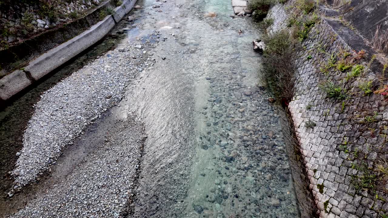Crystal clear water flowing gently through a low river, surrounded by smooth rocks and a sturdy stone wall in picturesque Japan