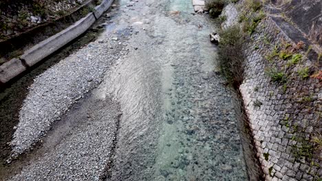 crystal clear water flowing gently through a low river, surrounded by smooth rocks and a sturdy stone wall in picturesque japan