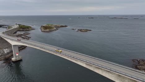 following two cars passing over storseisundet bridge along famous touristic atlantic ocean road in norway - aerial with north sea and atlantic ocean in background