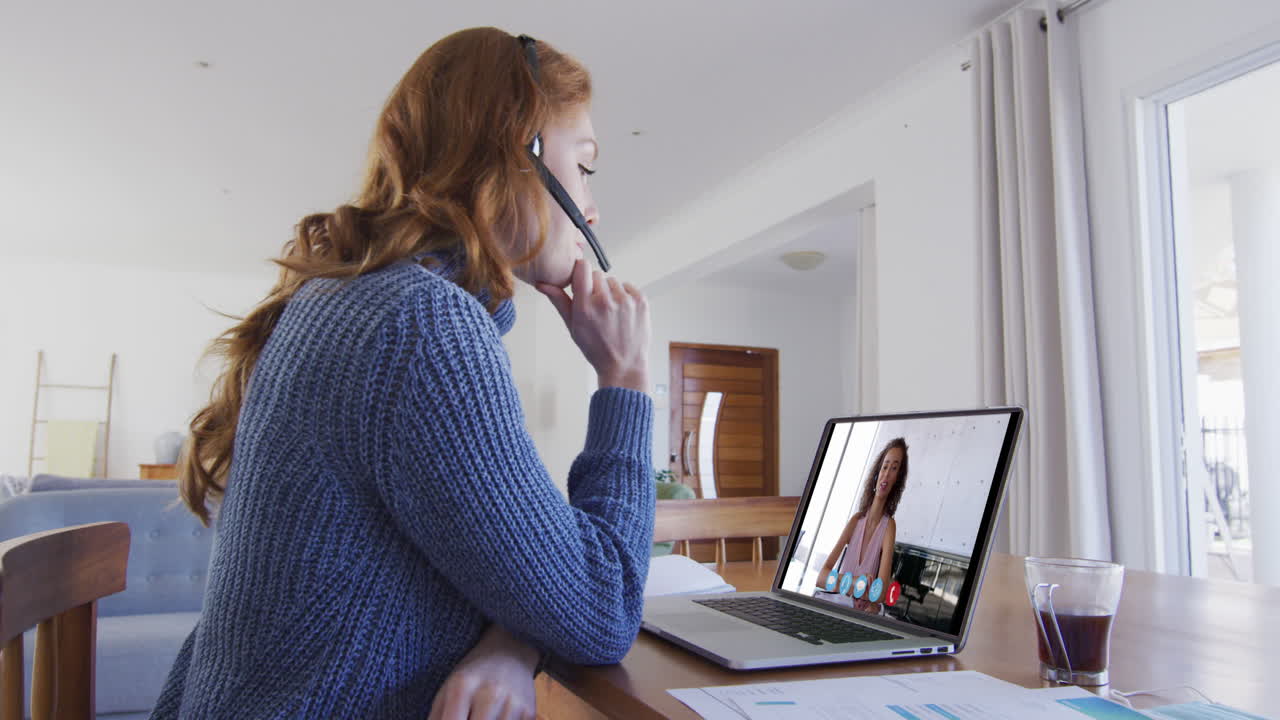 mujer caucásica usando portátil y auriculares de teléfono en videollamada con una colega