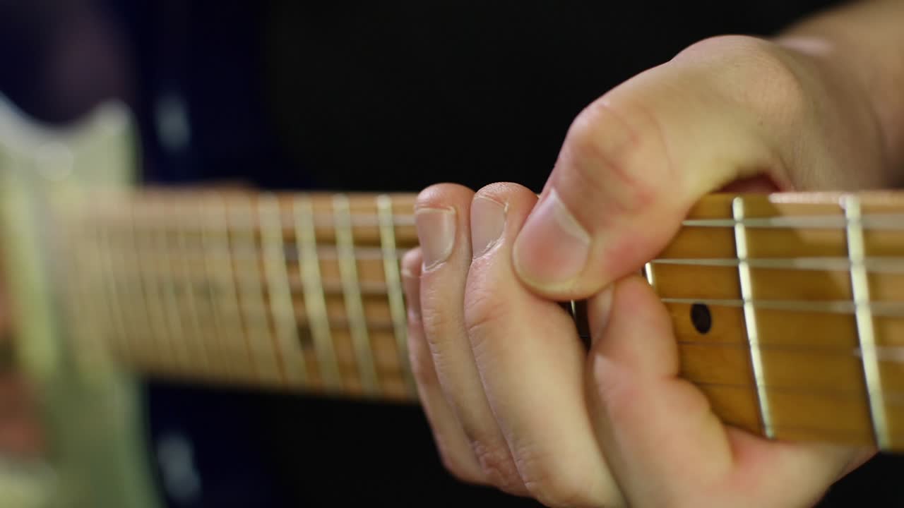 Slow motion close up of an electric stratocasters guitars neck and strings and guitarists hands while playing notes with a pick. Smooth slow motion with gimbal forward movement. Shot in 4K at 120fps