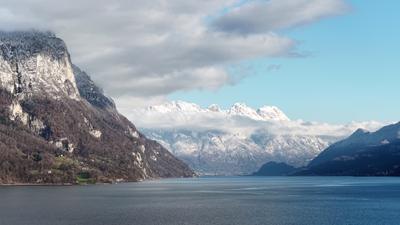 Aerial panorama over Walensee, Switzerland. Crystal blue water sits beneath snow-dusted cliffs and the Churfirsten range. A majestic winter landscape representing peace and natural beauty