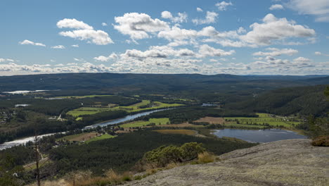 time lapse view of clouds moving over fields and forest, high up from a hill, sunny day, in south norway