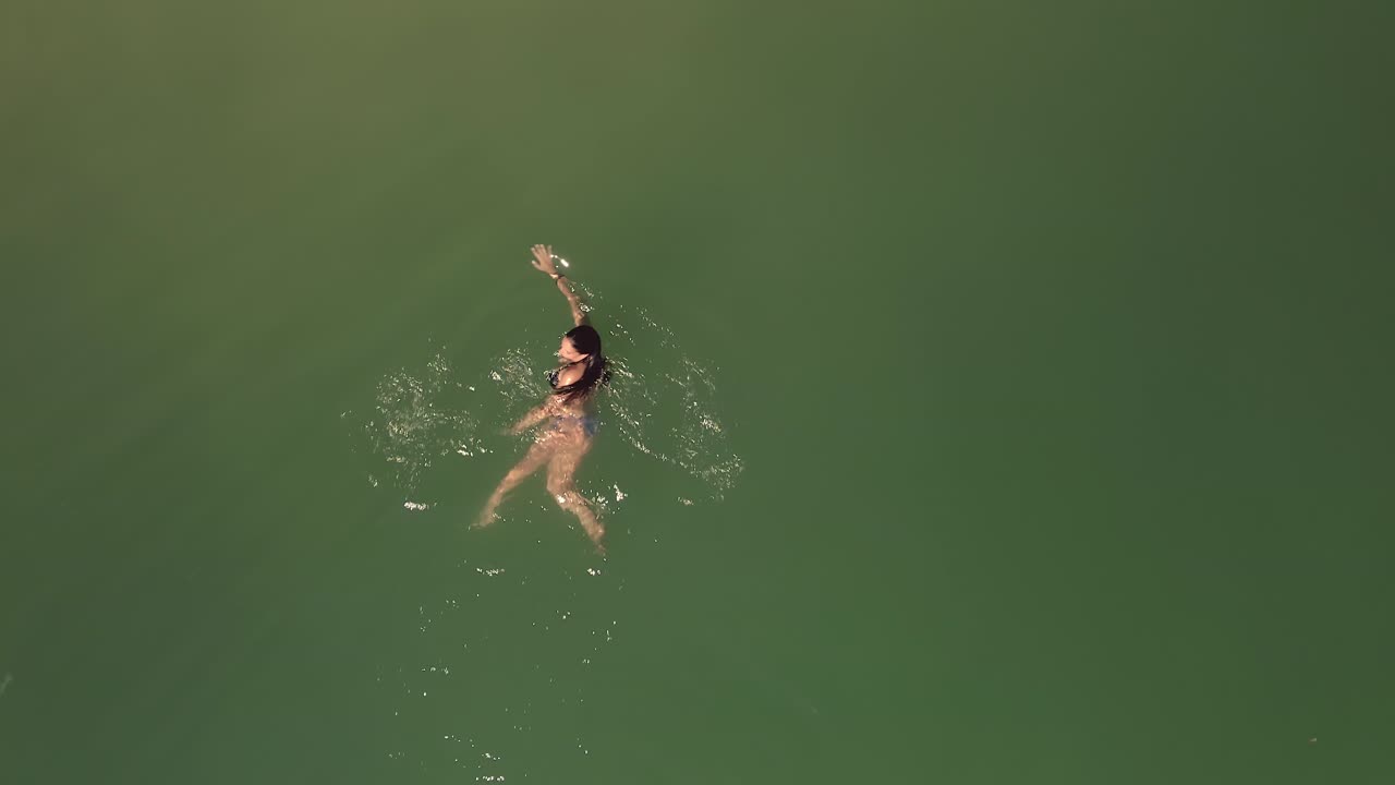 antena directamente encima de la mujer en bikini nadando en la hermosa superficie verde del océano