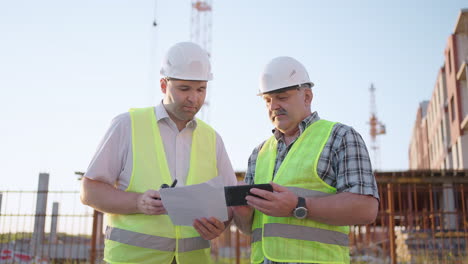 Zwei-Ingenieure-Diskutieren-Auf-Einer-Baustelle-über-Ein-Projekt.-Ein-Arbeiter-Trägt-Bei-Sonnenuntergang-Einen-Helm