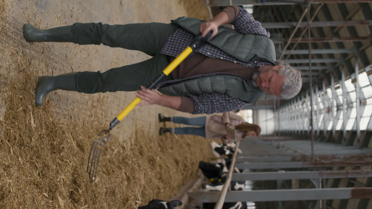 Vertical Shot of Man Shoveling Hay at Cattle Farm