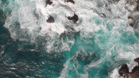 beautiful waves crashing against rocks with turquoise water pools - top down aerial rising drone shot