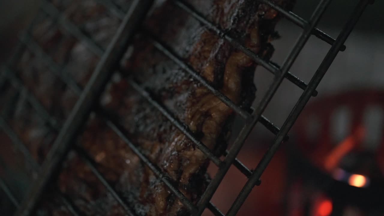 Close-up profissional de costelas de churrasco tradicionais argentinas cozinhando sobre fogo aberto. A profundidade de campo rasa destaca a textura da carne com um fundo de fogo brilhante e desfocado