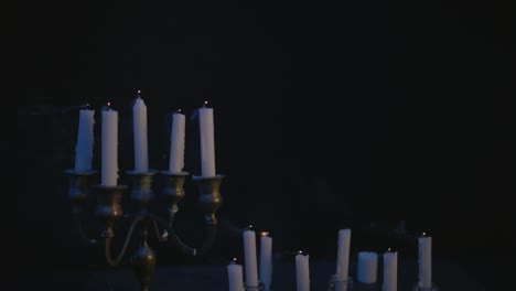 a group of white candles some on a candelabra lit up then blown out by the wind