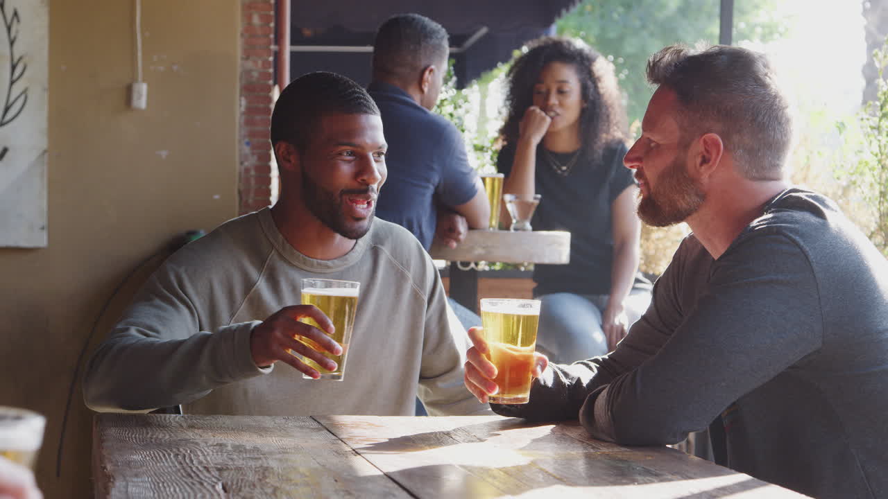 dos amigos se reúnen al aire libre en un bar deportivo disfrutando de una copa antes del juego