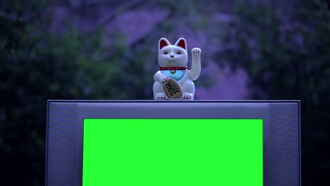 maneki neko cat or fortune cat over a retro tv with green screen. night tone. 4k.