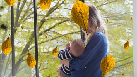 Animation-of-leaves-over-caucasian-mother-feeding-baby-in-park