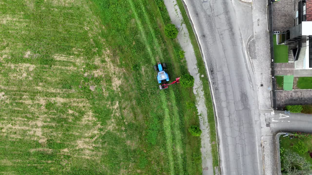 top down Aerial drone perspective capturing farmer cutting grass beside residential road, blending urban landscape with agricultural activity in Piacenza, Italian countryside