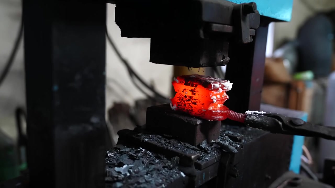 Power hammer compressing a white hot layered billet as scale and sparks fall away inside a knife making shop