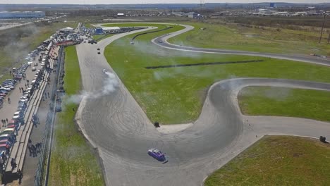 autos de carrera que van a la deriva en un giro con humo de neumáticos y espectadores clima soleado, plano general de un mapa