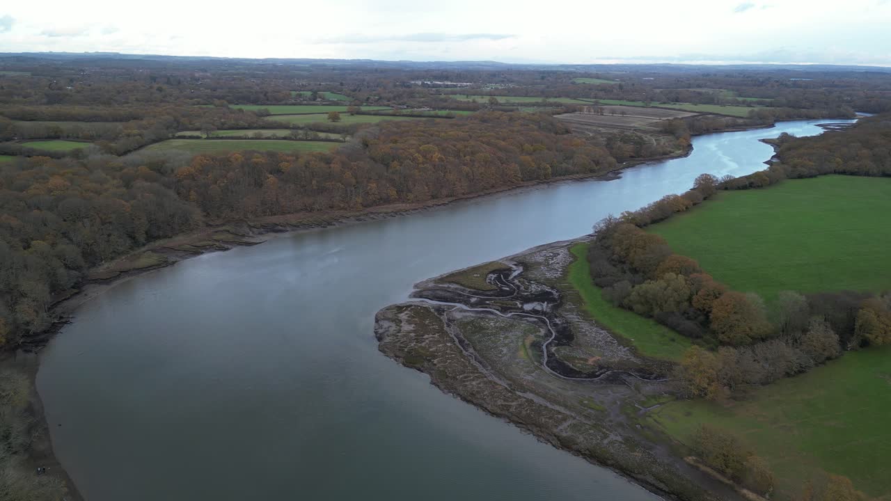 Aerial footage capturing the serene beauty of the Hamble River flowing through lush fields and woodland in Manor Farm Park, Hampshire. The crisp, clear view highlights autumn hues