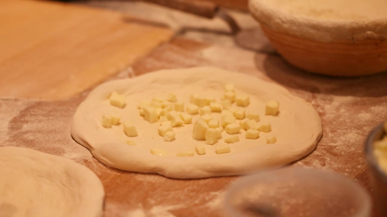 Chef professionista aggiunge cubetti di mozzarella all'impasto crudo della pizza su una superficie di legno infarinata.