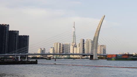 a static timelapse focusing on saigon river’s bridge and moving cargo vessels, capturing steady river traffic and urban activity without camera movement