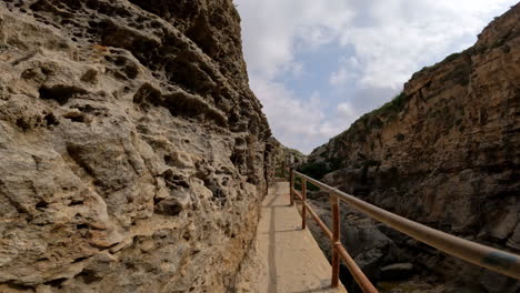 pov disparó mientras caminaba por un camino estrecho tallado en la ladera de piedra caliza con barandilla de hierro a lo largo de una pared de piedra amarilla y marrón en un día soleado