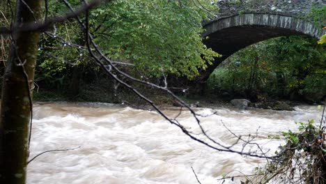 Rapid-flooding-flowing-river-water-under-idyllic-rural-arched-stone-bridge-dolly-right