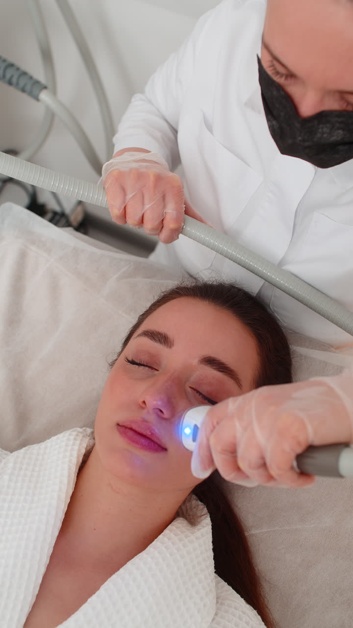 Caucasian woman gets rf facial massage by cosmetologist using electric device in beauty spa clinic