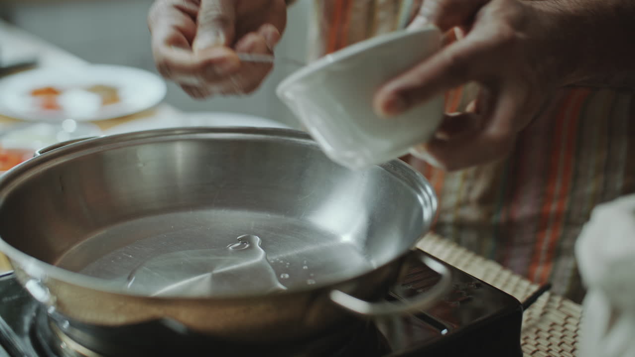 primer plano de las manos masculinas usando cuchara para verter aceite en la sartén calentada