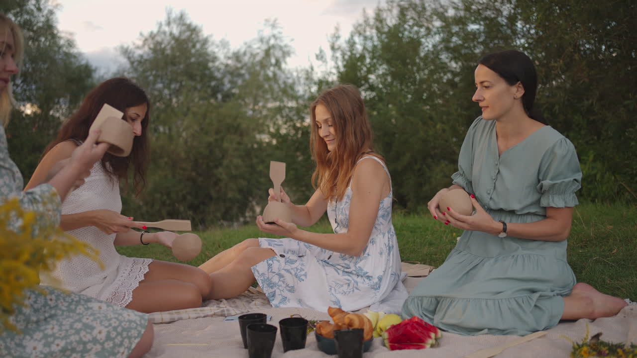 Young women in nature in the field in the park together sculpt clay with tools tap clay products with shovels communicate share their impressions. Joint creativity.