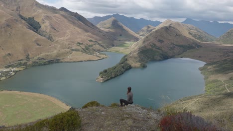 Junge-Kaukasische-Frau-Mit-Blick-Auf-Den-See-Zwischen-Den-Bergen,-Moke-Lake,-Queenstown,-Neuseeland