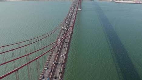 Luftneigung-Enthüllt-Den-Geschäftigen-Autoverkehr-Auf-Einer-Mehrspurigen-Straße,-Die-Die-Rote-Brücke-Ponte-25-De-Abril-In-Richtung-Stadtzentrum-Von-Lissabon,-Portugal,-überquert