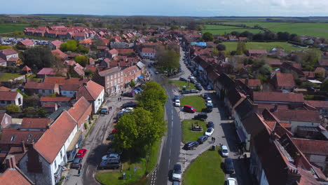 Un-Dron-Aéreo-Alto-Sobrevoló-El-Hermoso-Y-Antiguo-Mercado-De-Burnham-Con-Casas-Rojas-Y-Blancas-En-Un-Día-Soleado-Y-Nublado-Con-Gente-En-Las-Calles-Del-Norte-De-Norfolk,-Reino-Unido