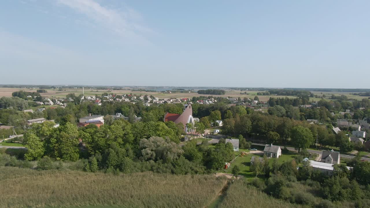 Drone flying to beautiful red roofed church and small town in forest and flatlands in background of Lithuania, aerial drone shot